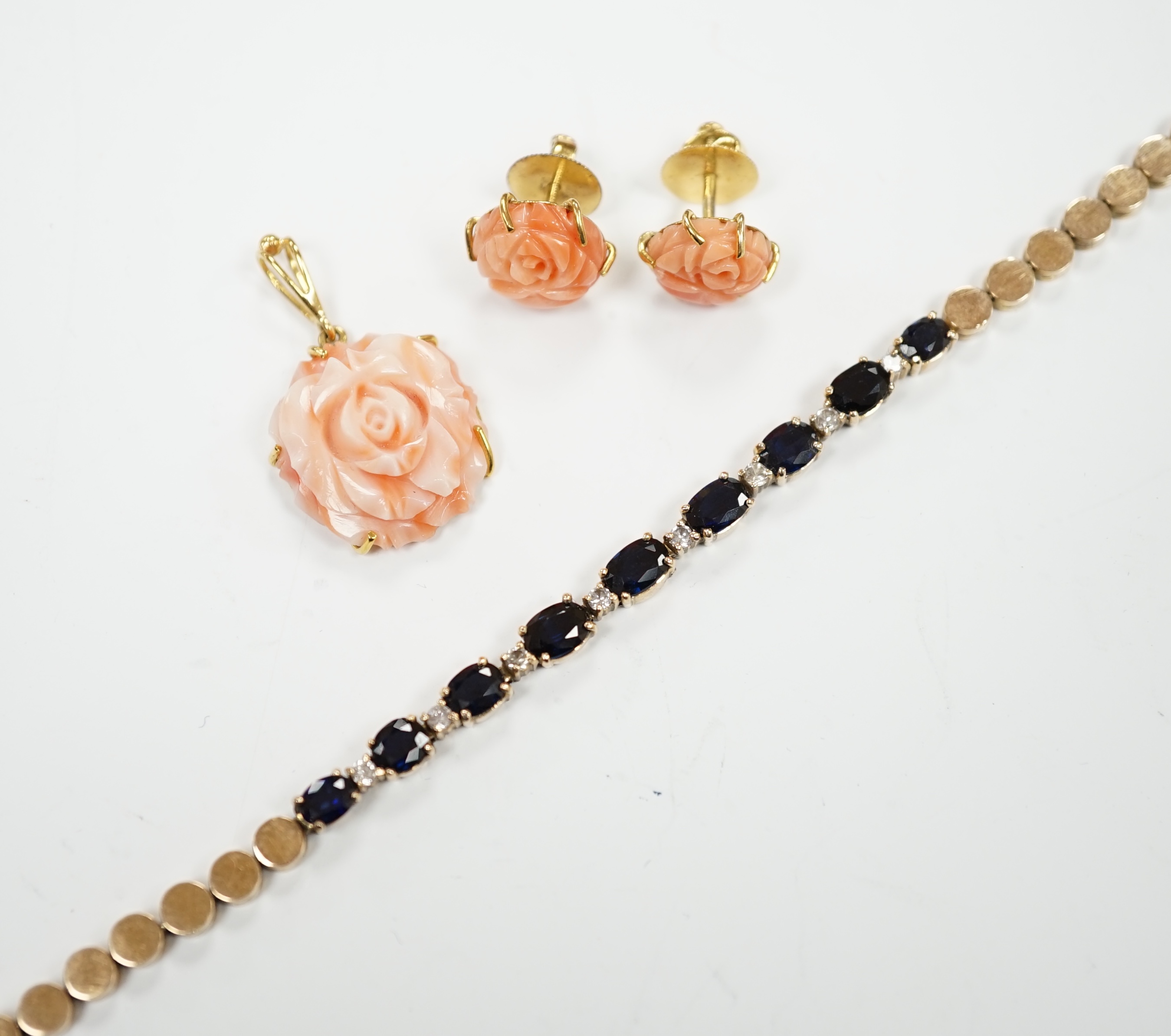 A modern 18ct and carved coral set 'rose' pendant, 16mm and a pair of matching ear studs and a yellow metal and two colour sapphire set line bracelet, 18cm.